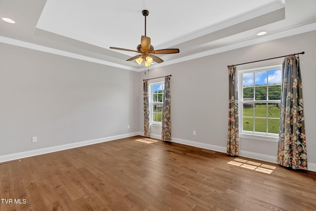 empty room with a tray ceiling, ornamental molding, wood finished floors, baseboards, and ceiling fan