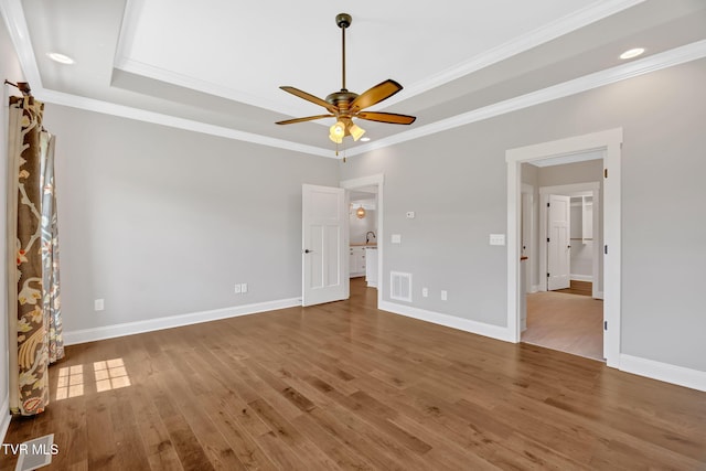 unfurnished bedroom featuring wood finished floors, crown molding, a tray ceiling, baseboards, and recessed lighting