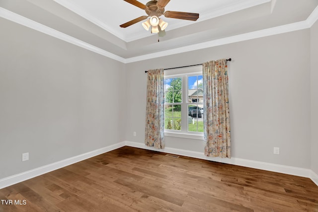 unfurnished room featuring a raised ceiling, wood finished floors, crown molding, a ceiling fan, and baseboards