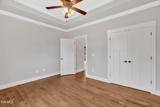 spare room with a tray ceiling, ornamental molding, wood finished floors, ceiling fan, and baseboards