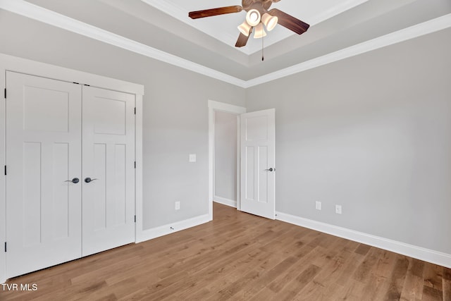 unfurnished bedroom with light wood finished floors, baseboards, a tray ceiling, ornamental molding, and a ceiling fan