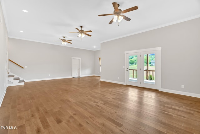 unfurnished living room featuring ceiling fan, wood finished floors, baseboards, crown molding, and stairs