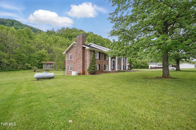 view of side of property featuring a chimney, brick siding, a lawn, and a view of trees