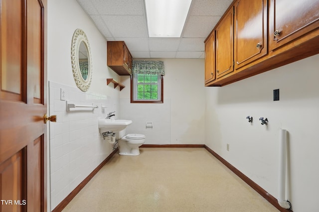 half bathroom featuring tile walls, toilet, a paneled ceiling, and a wainscoted wall