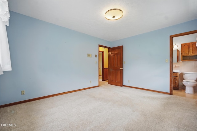 unfurnished bedroom with light colored carpet, baseboards, and connected bathroom