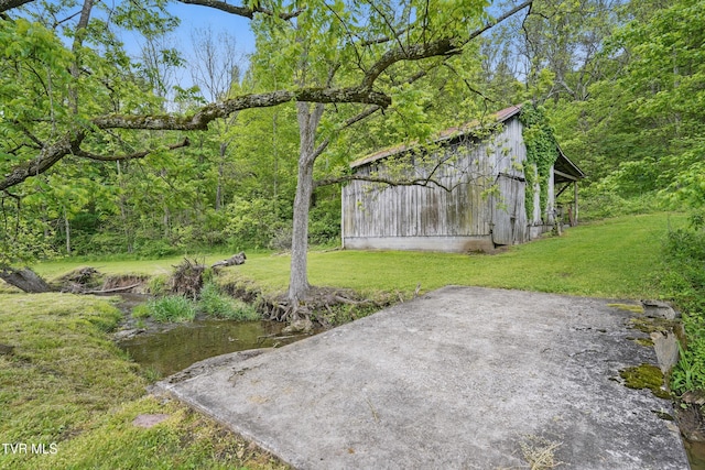 view of grassy yard featuring a barn, an outdoor structure, and a view of trees