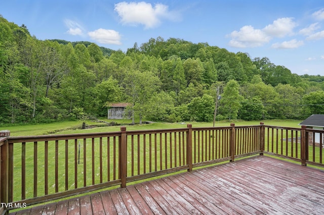 wooden deck featuring a view of trees, a lawn, an outbuilding, and a storage shed