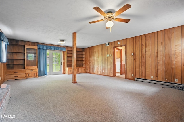 unfurnished living room with wood walls, carpet floors, a ceiling fan, a textured ceiling, and baseboard heating