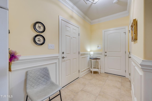 foyer with ornamental molding, wainscoting, light tile patterned floors, and a decorative wall