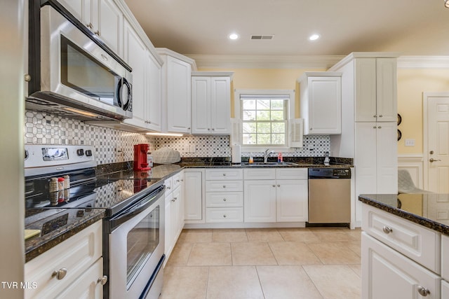 kitchen with appliances with stainless steel finishes, backsplash, ornamental molding, a sink, and dark stone countertops
