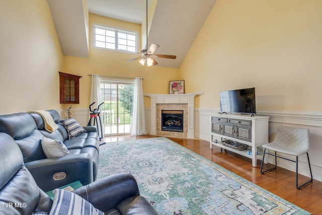 living room with a ceiling fan, wood finished floors, a glass covered fireplace, wainscoting, and high vaulted ceiling