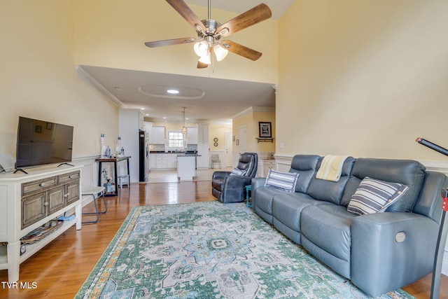 living room featuring a ceiling fan, ornamental molding, light wood finished floors, and a towering ceiling