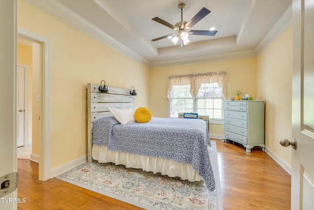 bedroom with a raised ceiling, light wood finished floors, crown molding, baseboards, and ceiling fan