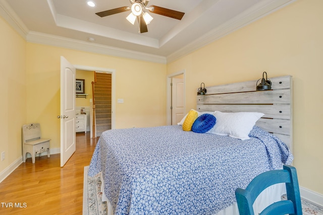bedroom featuring light wood-style floors, a raised ceiling, crown molding, and baseboards