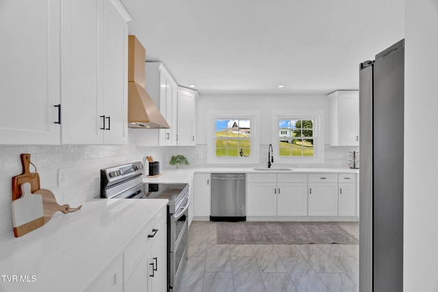 kitchen featuring stainless steel appliances, a sink, light marble finish floors, wall chimney exhaust hood, and backsplash