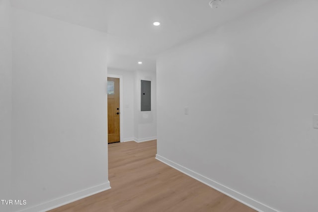 corridor featuring baseboards, recessed lighting, light wood-type flooring, and electric panel