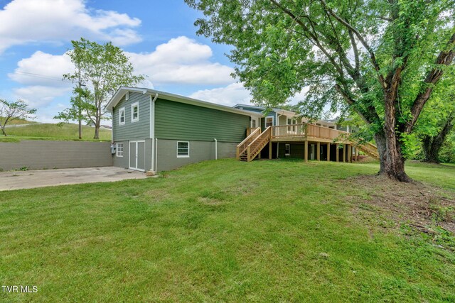 back of house featuring stairway, a wooden deck, driveway, a garage, and a lawn