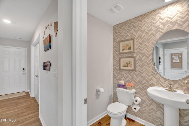 half bathroom with toilet, wood finished floors, a sink, and baseboards