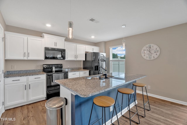 kitchen featuring black appliances, a center island with sink, light wood-style flooring, white cabinetry, and recessed lighting