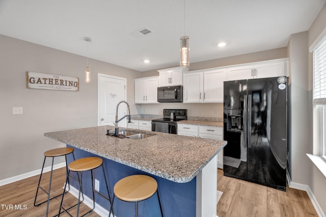 kitchen featuring black appliances, a sink, baseboards, white cabinets, and light wood-style floors