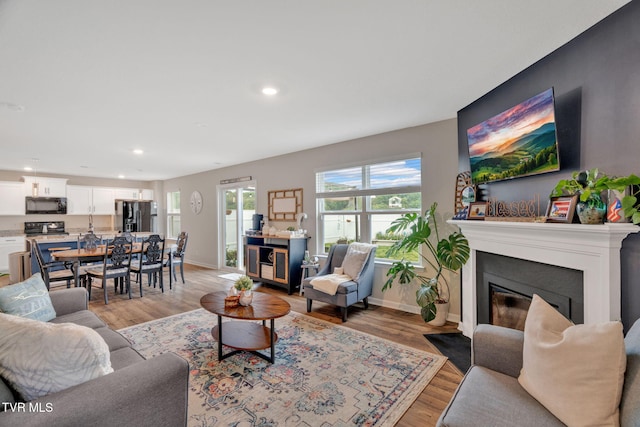 living room featuring recessed lighting, light wood-style floors, baseboards, and a fireplace with flush hearth