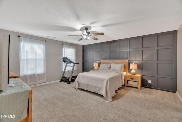 carpeted bedroom with a decorative wall, baseboards, ceiling fan, and a textured ceiling