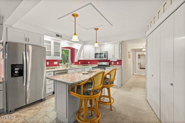 kitchen with stainless steel appliances, a sink, a breakfast bar area, white cabinetry, and glass insert cabinets