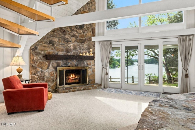 living room featuring plenty of natural light, high vaulted ceiling, carpet flooring, and a stone fireplace