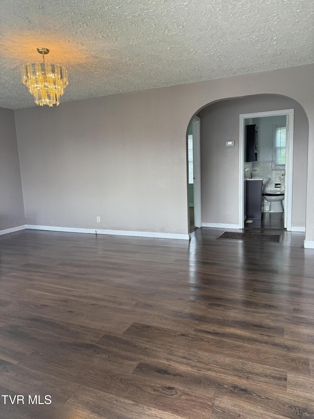 379 SW Oakland St, Abingdon, VA 24210 - spare room with arched walkways, a textured ceiling, a chandelier, dark wood finished floors, and baseboards