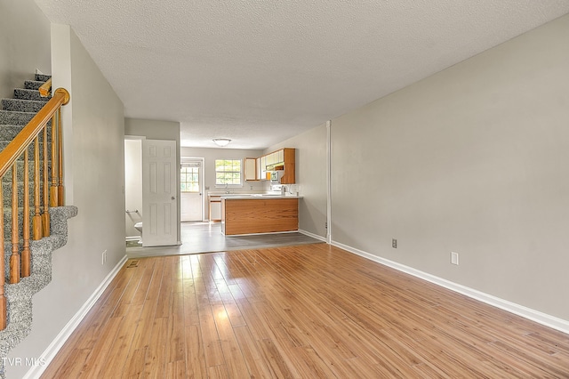 unfurnished living room featuring stairway, light wood finished floors, baseboards, a textured ceiling, and a sink