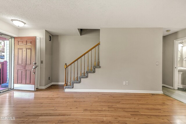 entrance foyer featuring light wood finished floors, a textured ceiling, baseboards, and stairway