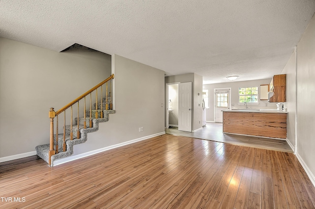 unfurnished living room with wood-type flooring, a textured ceiling, stairway, and baseboards