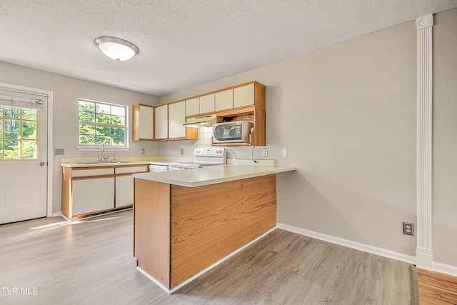 kitchen with white electric range oven, stainless steel microwave, a sink, light wood finished floors, and a peninsula