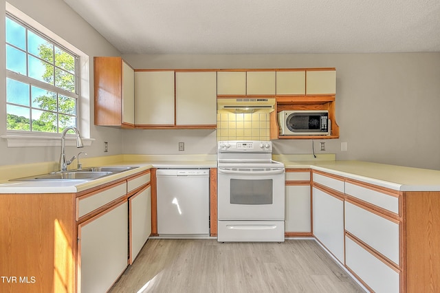 kitchen with white appliances, under cabinet range hood, light wood finished floors, a sink, and light countertops
