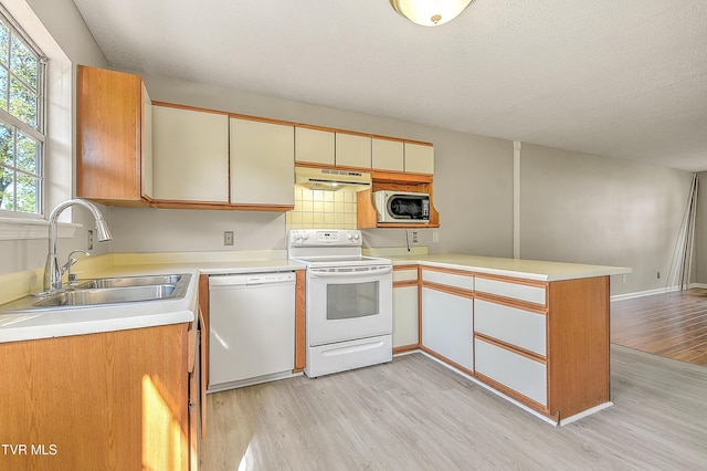 kitchen with white appliances, a sink, under cabinet range hood, a peninsula, and light wood finished floors