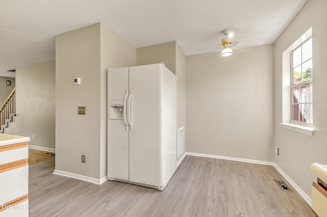 unfurnished room featuring light wood-style flooring, stairs, baseboards, and a textured ceiling