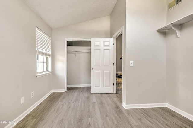 unfurnished bedroom with vaulted ceiling, wood finished floors, a closet, a textured ceiling, and baseboards