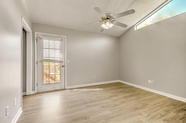 empty room featuring ceiling fan, light wood-style flooring, a textured ceiling, baseboards, and vaulted ceiling