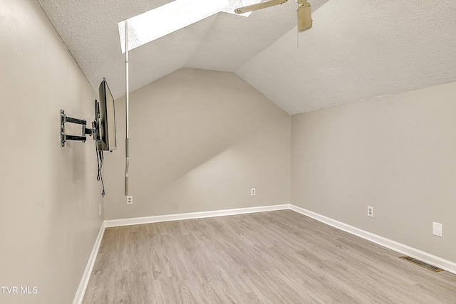 additional living space featuring a skylight, wood finished floors, a textured ceiling, lofted ceiling, and baseboards