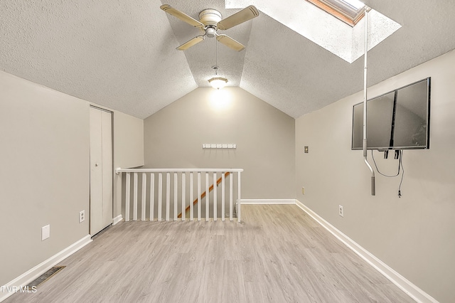 additional living space featuring a textured ceiling, wood finished floors, a skylight, ceiling fan, and baseboards