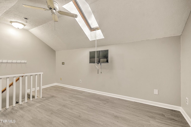 additional living space featuring a textured ceiling, a ceiling fan, vaulted ceiling, a skylight, and wood finished floors