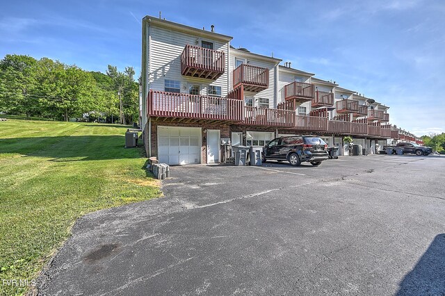 back of property featuring central air condition unit, a balcony, a yard, and an attached garage