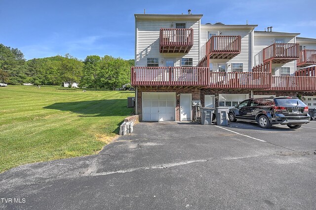 rear view of property featuring a lawn, an attached garage, and asphalt driveway
