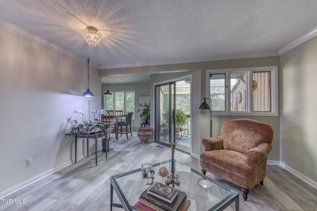 living room with a textured ceiling, wood finished floors, ornamental molding, baseboards, and a chandelier