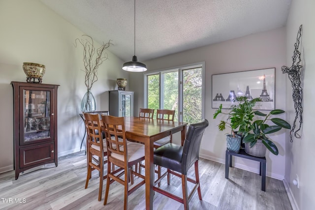 dining area featuring a textured ceiling, light wood-style flooring, and baseboards