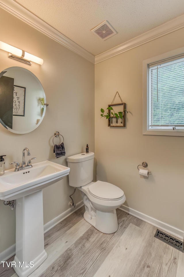 half bathroom featuring wood finished floors, toilet, ornamental molding, baseboards, and a textured ceiling