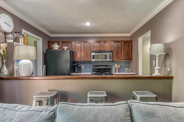 kitchen with freestanding refrigerator, stainless steel microwave, stove, crown molding, and decorative backsplash