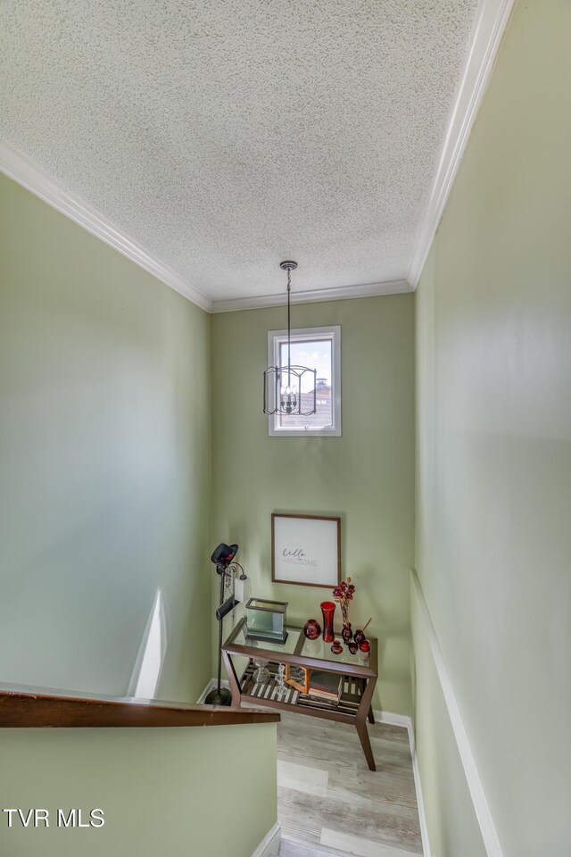 staircase with a textured ceiling, ornamental molding, wood finished floors, a chandelier, and baseboards