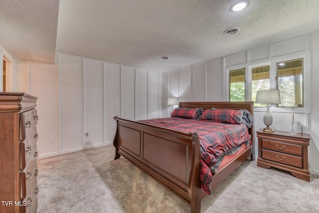 bedroom with a textured ceiling, a decorative wall, and light colored carpet