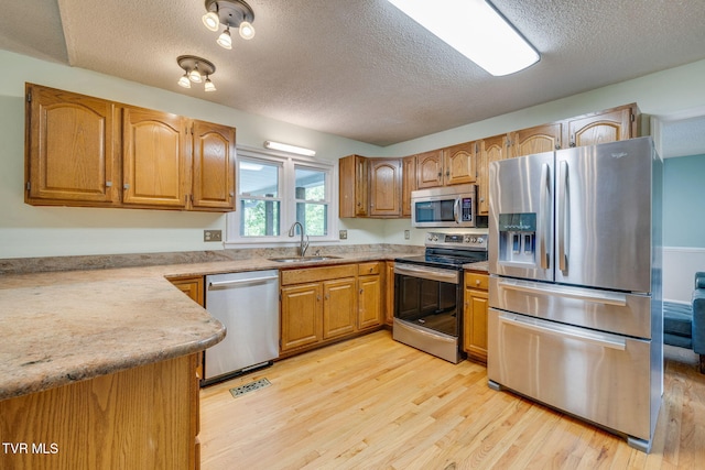 212 Old Castle Rd, Kingsport, TN 37660 - kitchen featuring appliances with stainless steel finishes, a sink, light wood-style floors, a textured ceiling, and brown cabinetry